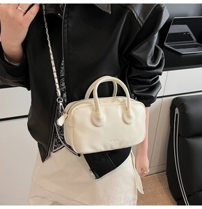 Detail of a creamy white mini bowling bag with chain strap worn by a modern woman