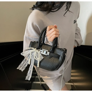 Close-up of black litchi leather bag with white lace bow and pearl charms on silver handle