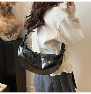 Detail of black faux leather dumpling bag with knotted strap and vertical stitching accents