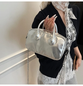 Detail of silver metallic bowling bag with chain strap and branding on black knitwear