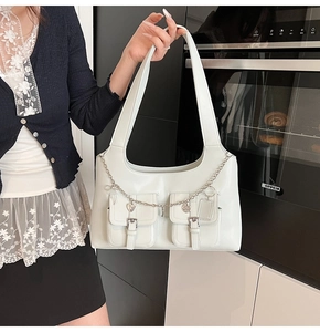Detail of cream white PU leather tote with dual buckle pockets and heart chain charm