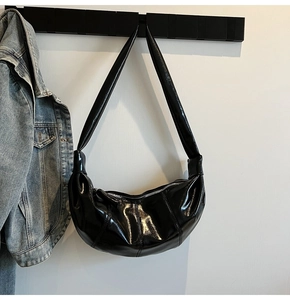 Detail of black glossy leather crescent bag with stitching and wide shoulder strap