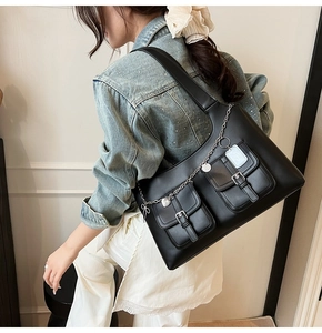 Detail of black leather commuter tote bag featuring dual flap pockets and silver metal chains