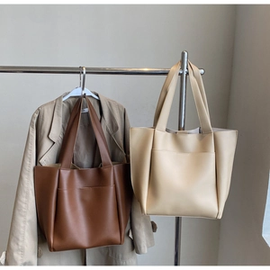 Detail of dark brown and beige leather tote bags with wide straps on a metal hanger