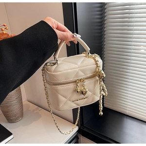 Détail du sac cylindrique matelassé crème avec chaîne dorée et breloques cœur