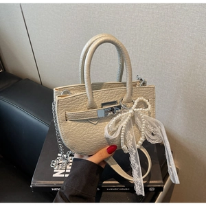 Detail of cream crossbody bag with lychee texture, pearl bow charm, and silver hardware