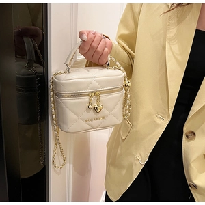 Détail du sac cylindrique matelassé beige avec chaîne dorée et breloque en cœur
