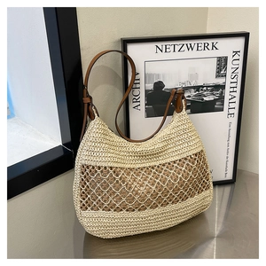 Detail of hollow woven straw shoulder bag with brown faux leather strap and crescent shape