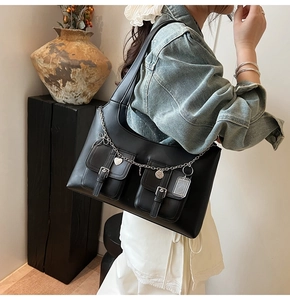 Detail of black faux leather tote featuring front buckled pockets and silver heart charms