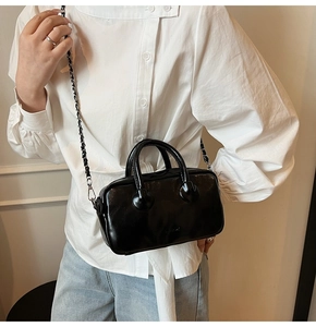 Detail of a black glossy mini bowling bag with chain strap worn by a model