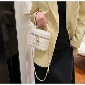 Détail du sac cylindre blanc matelassé avec fermeture cœur et bandoulière chaîne