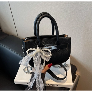 Detail of black pebbled leather bucket bag with silver twist lock and pearl lace charm