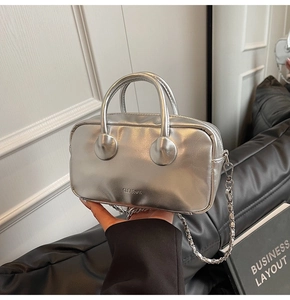 Detail of silver metallic bowling bag with chain strap on black leather sofa