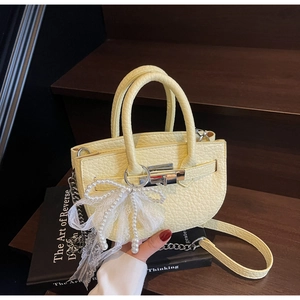 Detail of light yellow lychee leather bucket bag with silver hardware and lace bow charm