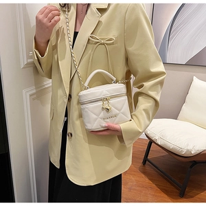 Détail d'un sac cylindre blanc matelassé avec pendentif cœur doré et bandoulière chaîne