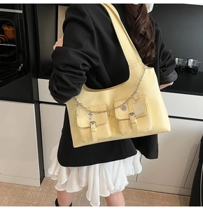 Detail of bright yellow leather tote bag with double buckled pockets and metal heart chain