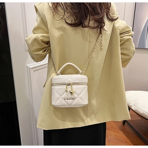 Détail d'un sac cylindrique blanc matelassé avec breloques cœur dorées et bandoulière
