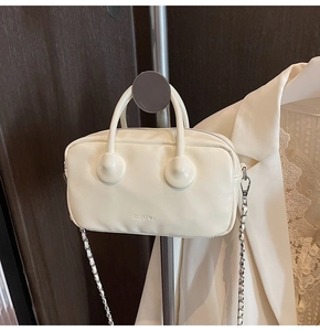 Detail of a creamy white leather bowling bag with CLEARK embossed logo and chain strap