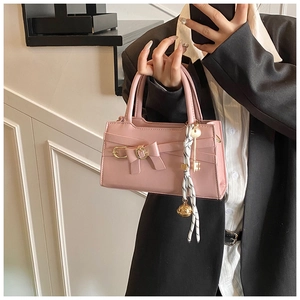 Detail einer rosa Handtasche mit großer Schleife und goldenem Schlüsselanhänger-Akzent