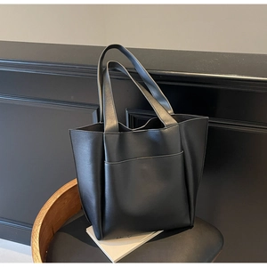 Minimalist black tote bag with front pocket displayed on a leather chair in a dark setting
