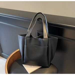 Detail of a black matte leather tote bag featuring a front pocket and handle on a chair