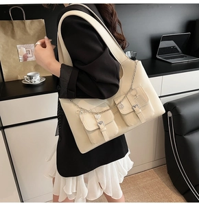 Detail of cream tote bag with dual front pockets and silver heart chain charm
