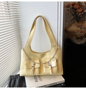 Detail of light yellow tote bag featuring dual front pockets and silver heart chain charm