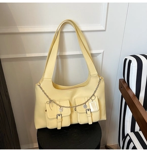 Close-up of cream yellow tote bag featuring front utility pockets and silver chain charms