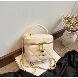 Détail du sac cylindre matelassé crème avec chaîne dorée et pendentif en cœur
