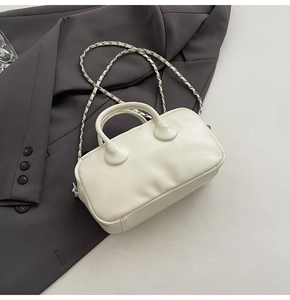 Detail of cream white leather bowling bag with metallic chain strap on gray blazer