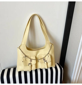 Detail view of the yellow faux leather shoulder bag featuring buckled pockets and heart chain