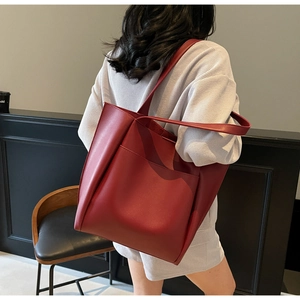 Model wearing a large burgundy matte leather tote bag with a minimalist front pocket
