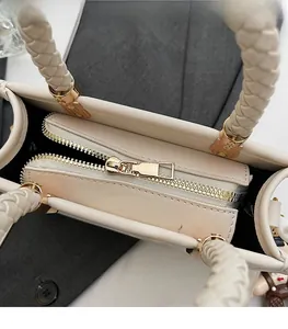 Detail of light gold zipper and woven handle on a beige square handbag with plush charm