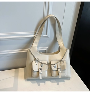 Detail of cream white tote bag featuring front buckle pockets and silver charm chain