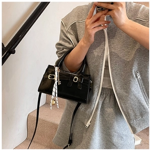 Schicke schwarze Lackledertasche mit Schleife und gestreiftem Schal an einem Model
