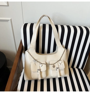Detail of a creamy white tote bag with silver buckles and decorative heart chain