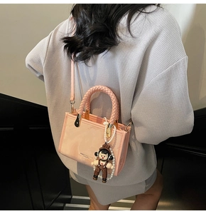 Close-up of pink crossbody bag with woven handle and cute pearl doll charm detail