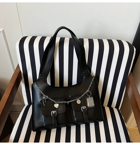 Detail of black leather tote bag with silver chains, heart pendants, and double front pockets