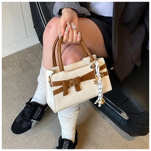 Detailaufnahme der Kontrast-Tasche mit Schleife, Goldschnalle und geflochtenem Anhänger