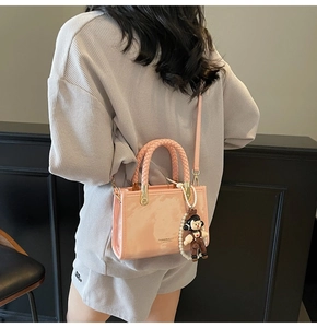 Pink glossy leather crossbody bag with beaded charm and adjustable strap detail