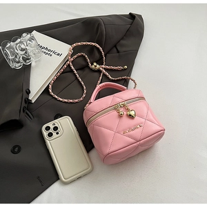 Détail du mini sac cylindrique rose matelassé avec chaîne dorée et breloque cœur près du tel