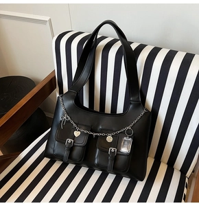 Detail of black PU leather tote with silver heart pendants and chain on striped sofa
