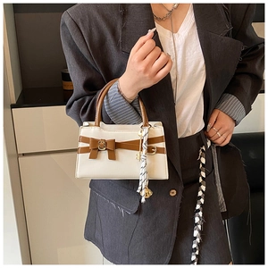 Detail einer weißen quadratischen Handtasche mit braunen Griffen und goldenem Glöckchen