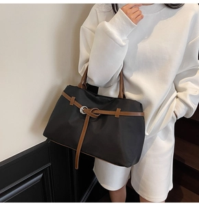 Detail of the black tote bag with brown leather straps and metal ring buckle design