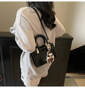 Detail of black patent leather handbag with woven handle, pearl charm and white lettering