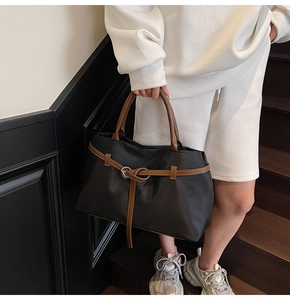 Detail of black nylon tote bag with brown leather handle and metal buckle strap design