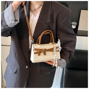 Detail einer schicken quadratischen Handtasche mit brauner Schleife und Schlüsselanhänger