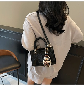 Detail of black patent leather crossbody bag with woven handle and pearl charm