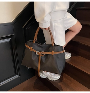 Detail of a large black nylon tote bag with brown leather handles and metal ring accents