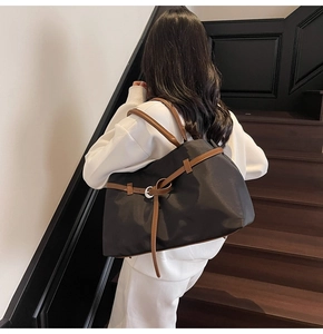 Side view of large black tote bag with brown leather straps and knot detail on a model